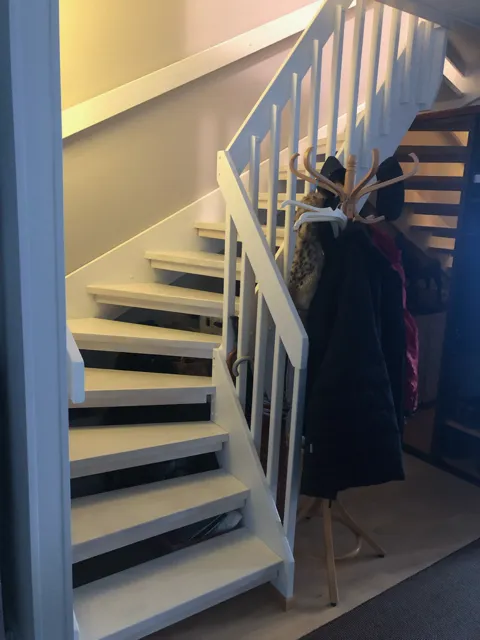 Valkoiset portaat johtavat yläkertaan, vieressä vaatenaulakko ja takkeja. Valoisa ja moderni sisustus.