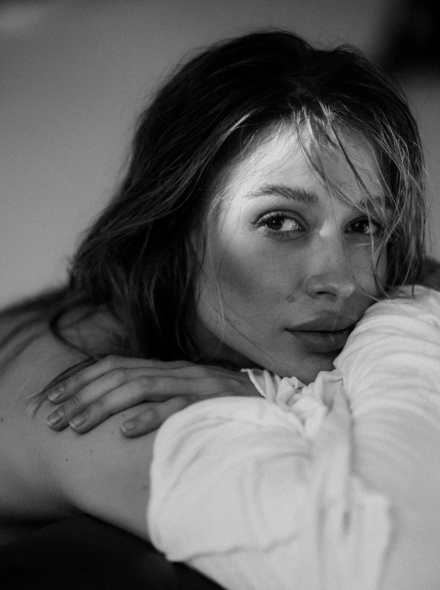 Чорно-біле портретне фото жінки із розпущеним волоссям, яка лежить із рукою на плечі і дивиться у камеру.