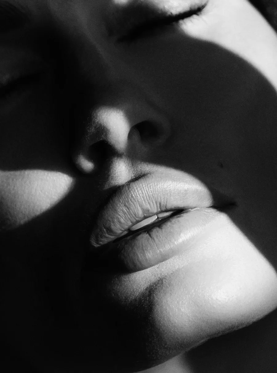 Крупний план обличчя з закритими очима, зосереджений на губах і носі в чорно-білому кольорі.