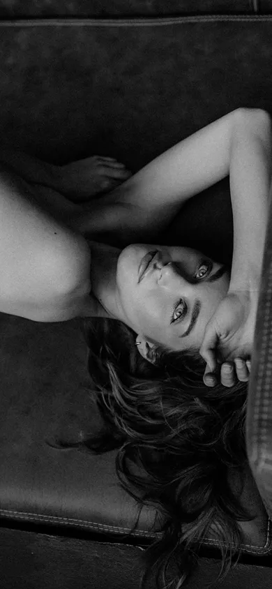 Жіночий портрет у чорно-білому стилі, де жінка лежить, піднявши руку до голови і дивиться в камеру.