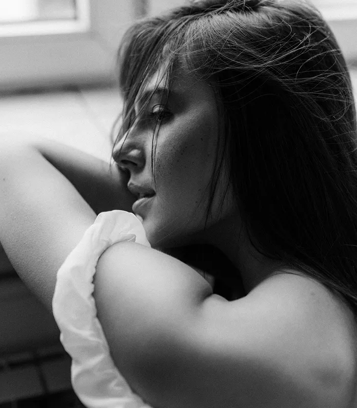 Чорно-білий портрет жінки в профіль з розпущеним волоссям біля вікна.