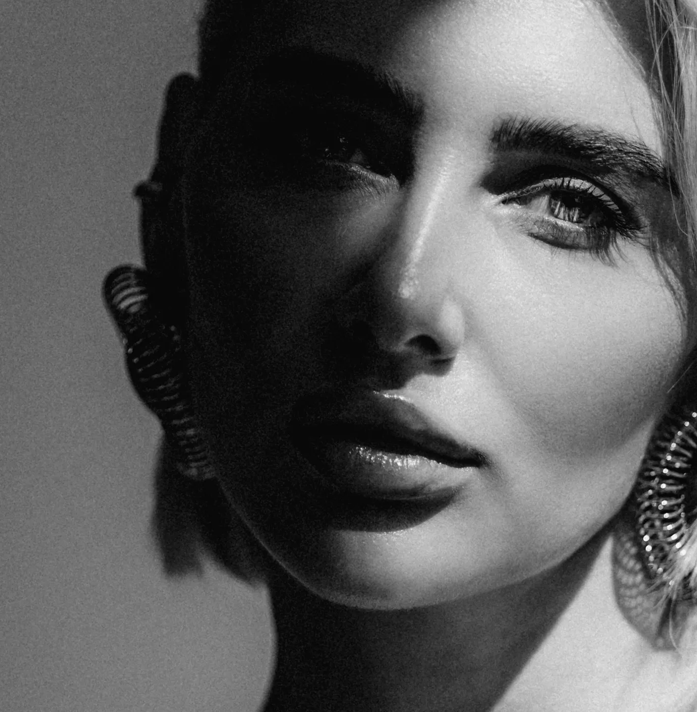 Чорно-біле крупним планом жіночого обличчя з виразними очима та великими сережками.