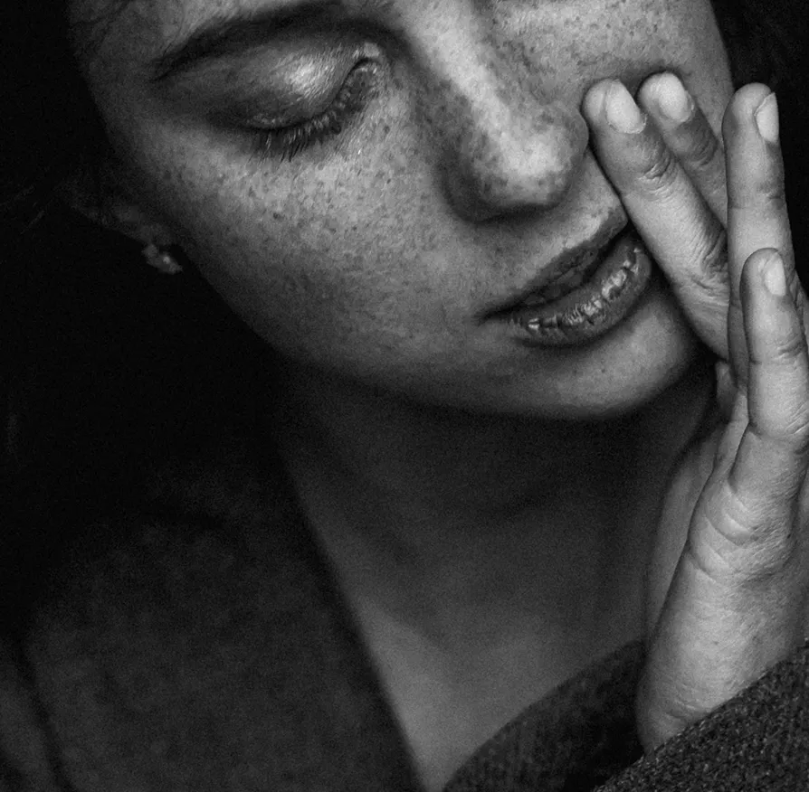 Чорно-білий портрет жінки з веснянками, очі закриті, рука доторкається до обличчя.