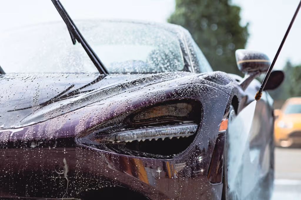 Close-up of a shiny black sports car headlight being washed with water spray and soap suds.