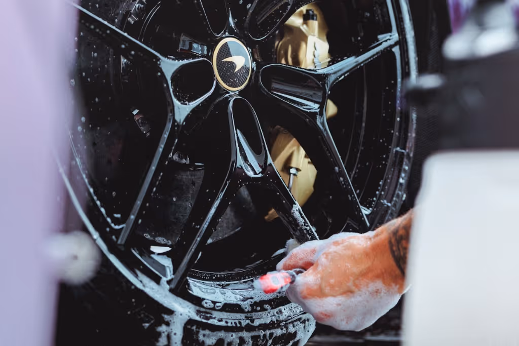 Person cleaning black McLaren car wheel with soap and a small brush.