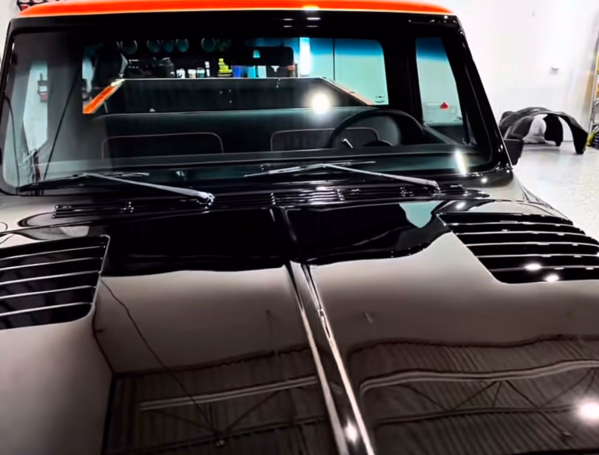 Close-up front view of a shiny black classic car with an orange roof in a garage.