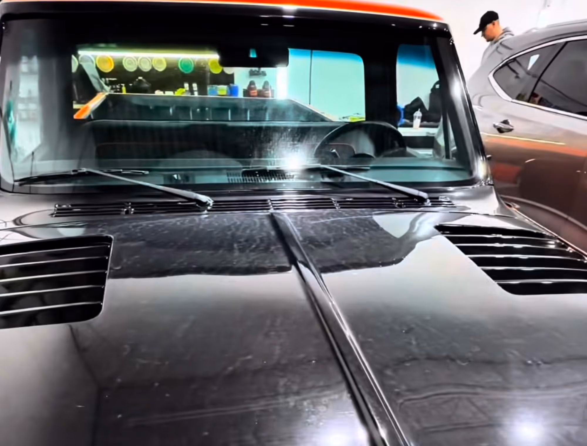 Front view of a black vintage car hood with vents and windshield wipers in a garage.