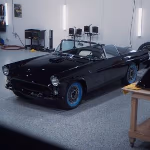 Black vintage convertible car with blue wheels parked inside a clean garage.