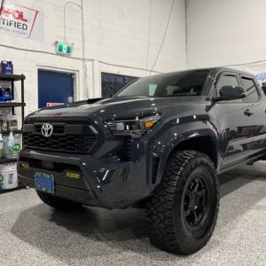 Black Toyota Tacoma truck with large off-road tires parked inside a garage.