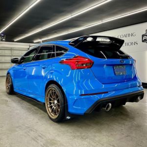 Blue sporty hatchback car with a large rear spoiler parked indoors under ceiling lights.