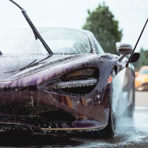 Close-up of a purple sports car being washed with water and raised windshield wipers.