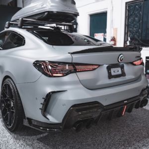 Rear view of a matte gray sports car with custom taillights and four exhaust tips parked inside a garage.