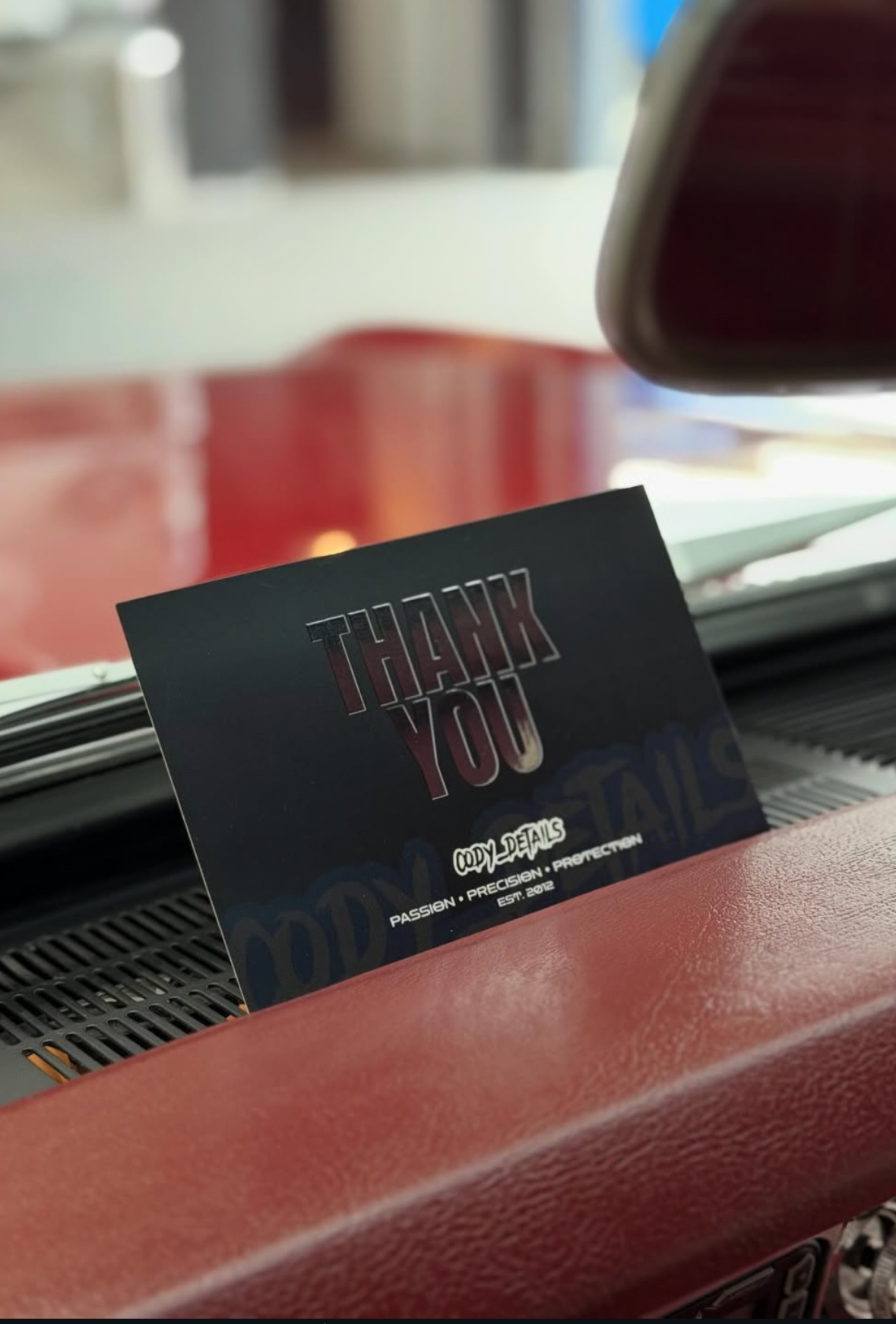 Business card with THANK YOU message resting on red car interior near windshield.