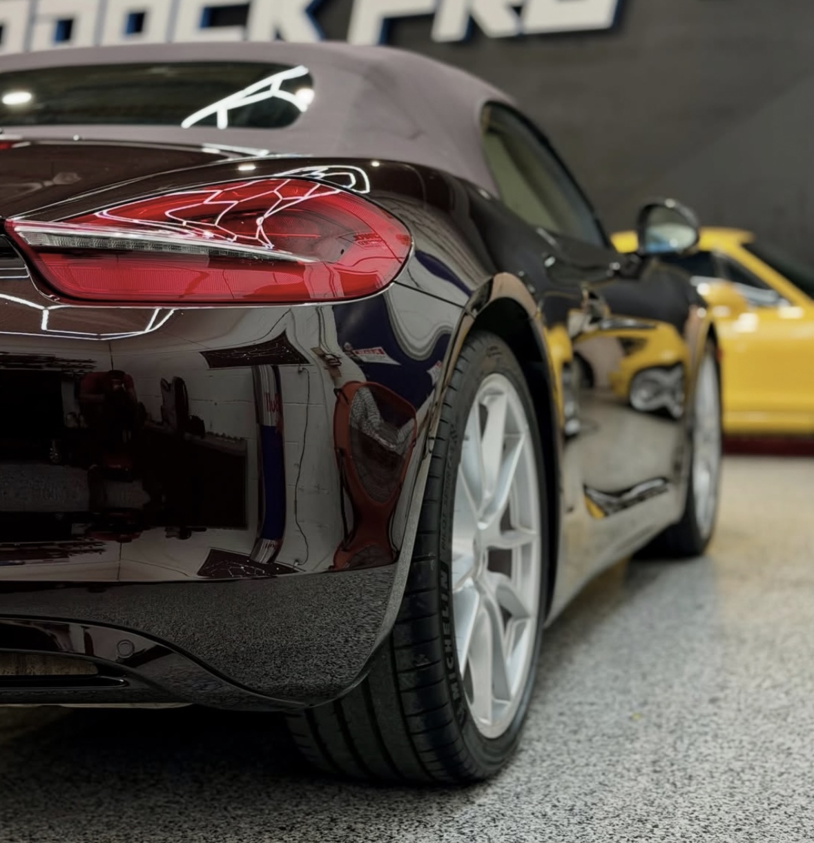 Close-up of a black sports car's rear with detailed taillight, tire, and blurred yellow car in background.