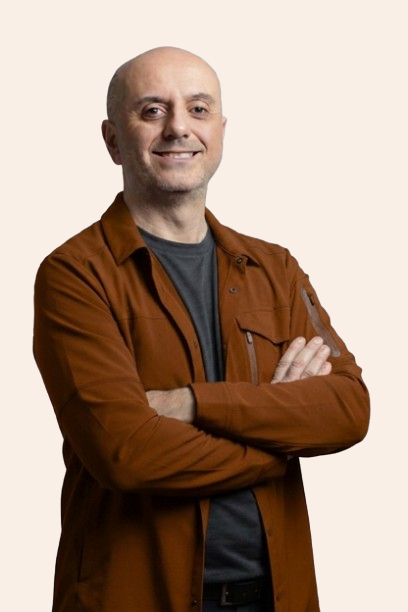 Smiling man in a brown jacket with arms crossed on a light background.