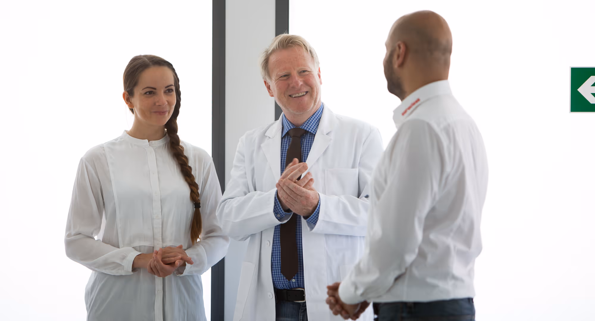 Drei lächelnde Personen, ein Arzt in Arztkittel mit seiner Assistentin in weißen Hemden, im Gespräch mit Euroclean Geschäftsführer Goran Sperac in einem hellen Raum.