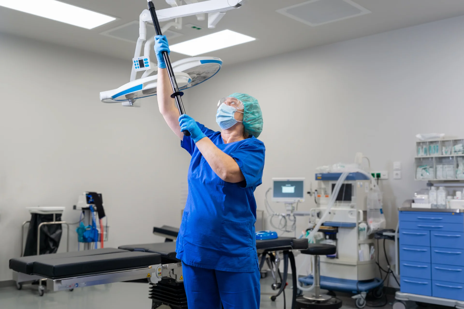 Medizinische Fachkraft in blauer Schutzkleidung stellt eine OP-Lampe in einem Operationssaal ein.