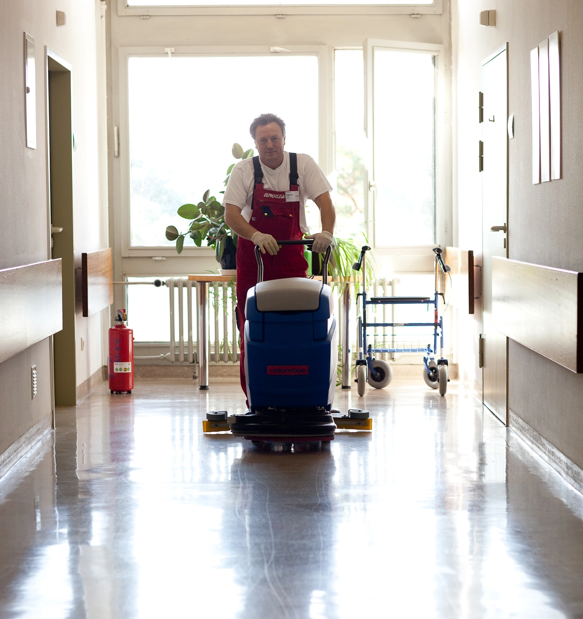 Männliche Reinigungskraft von Euroclean reinigt glänzenden Flur mit einer Bodenreinigungsmaschine in einem Gebäude.
