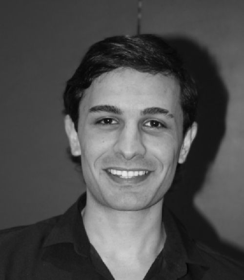 Smiling young man with dark hair wearing a collared shirt against a plain background.
