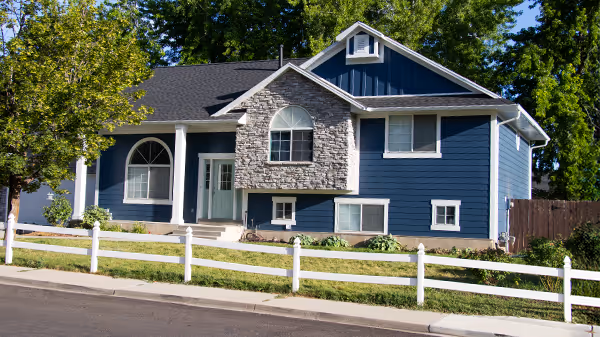 Blue split-level house with stone facade accent, white trim, and a white fence along the front yard.