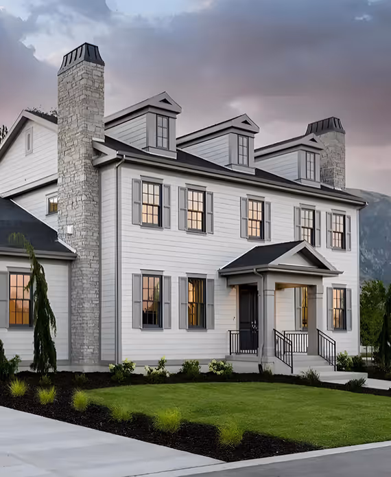 Large two-story white house with gray shutters, two stone chimneys, and a manicured front lawn at dusk.