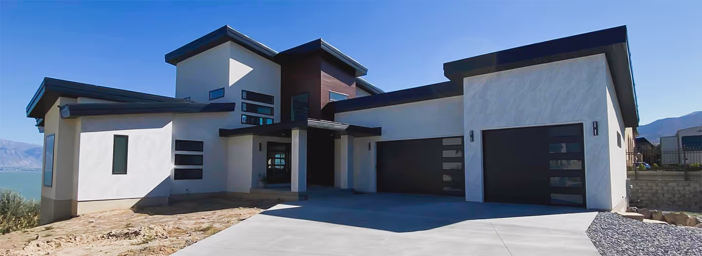 Modern two-story house with white and dark exterior walls, large garage doors, and a concrete driveway under a clear blue sky.