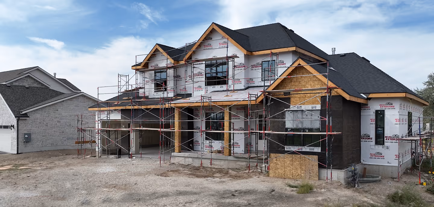 Large house under construction with scaffolding around the front and partially installed exterior materials.