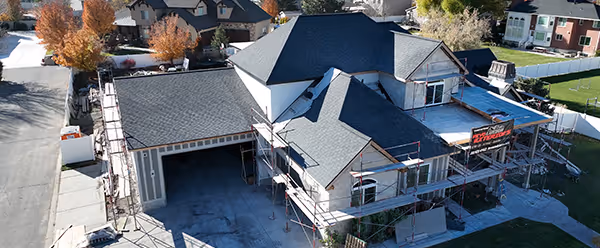 A large house under construction with new dark gray roofing and scaffolding around it.