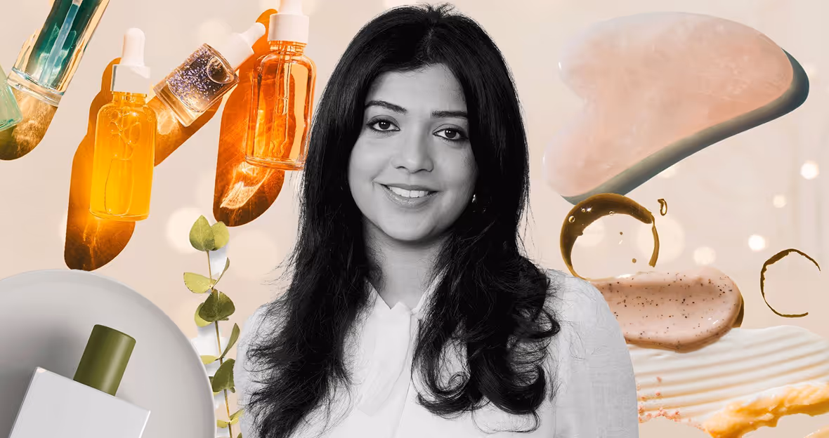 Smiling woman with long black hair in white blouse surrounded by skincare serum bottles, a gua sha tool, and cosmetic cream textures.