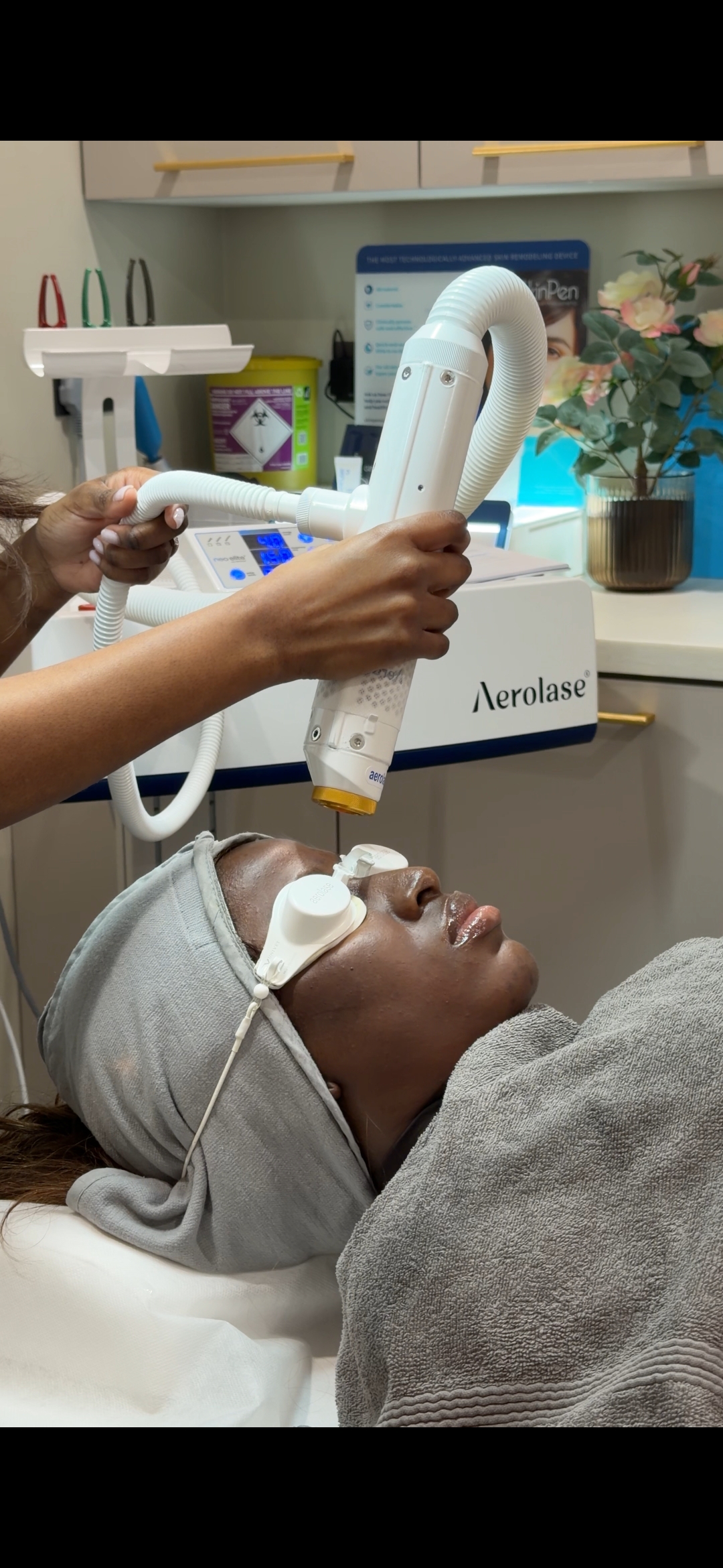 Smiling woman with black hair applying cream to her cheek, wearing a white shirt and a silver ring with a crescent moon design.