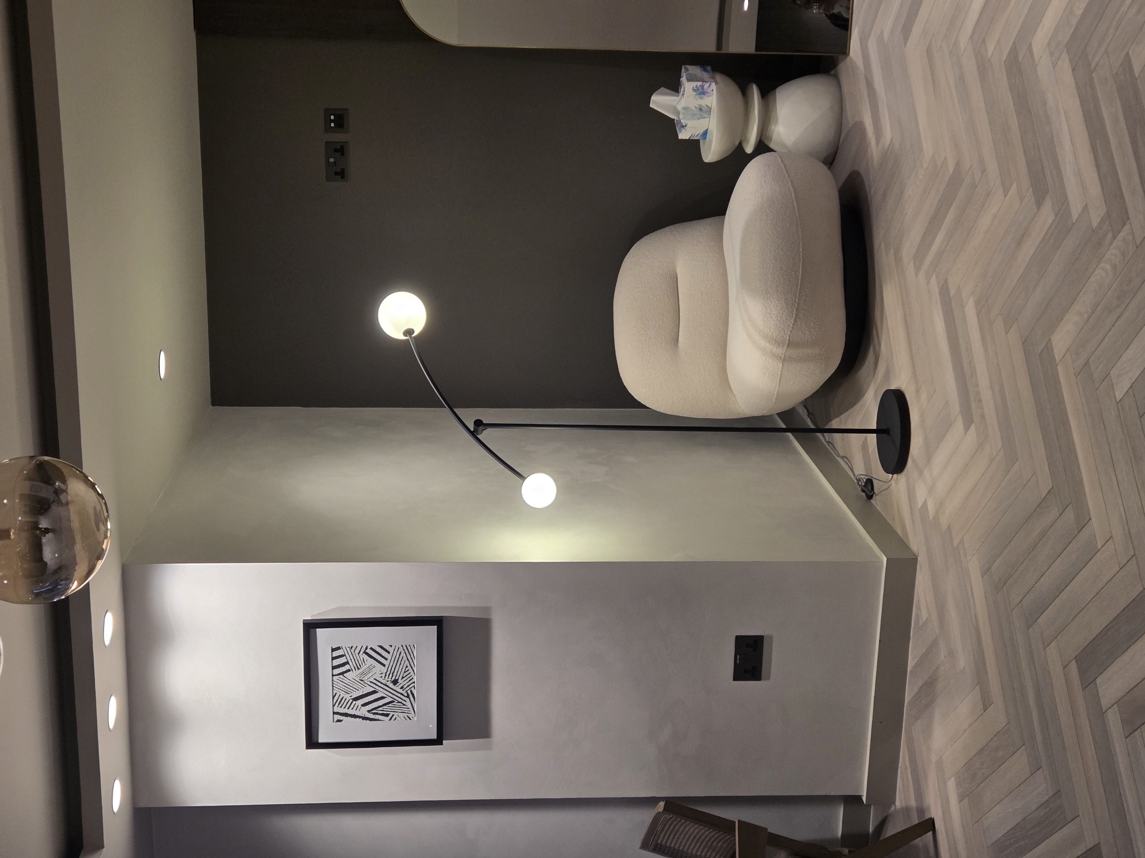 Modern curved reception desk with a silver Apple computer, a flower vase, hand sanitizer, and a small photo frame in a brightly lit office.