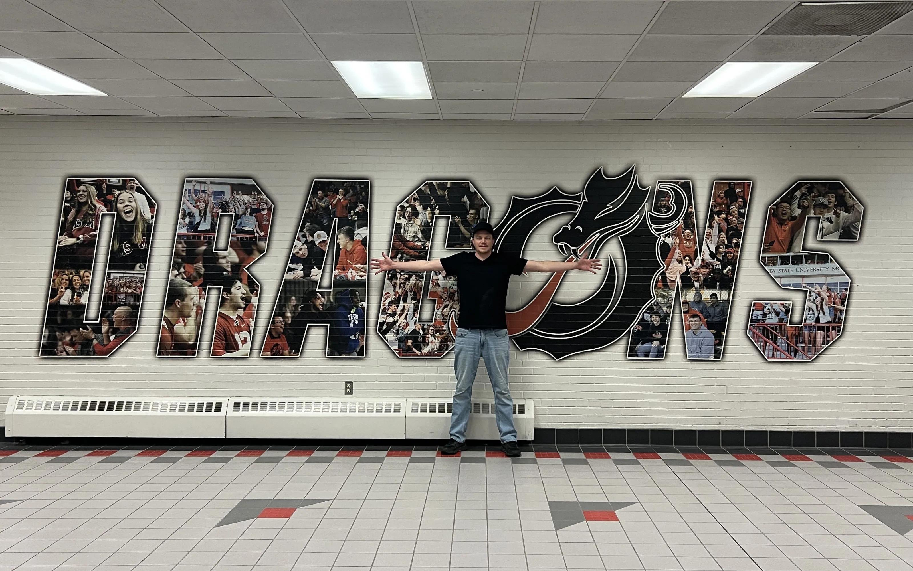 Man standing with his arms spread wide to show the scale of a mural printed with a wall printer.