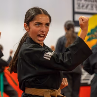 Young martial artist in a black uniform with a brown belt performing a strong punch with an intense expression in Temecula, CA at the United Studios of Self Defense Temecula dojo.