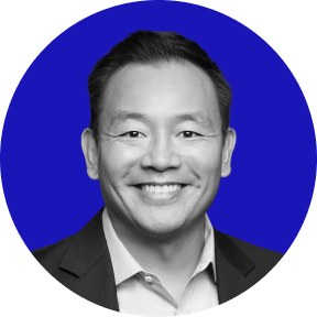 Headshot of a smiling man wearing a suit jacket and collared shirt with a solid blue circular background.