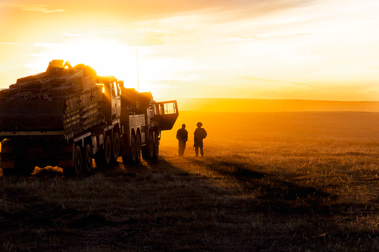 Military logistics vehicles in a field at sunset with two soldiers, from Al Topping's Army engineering career