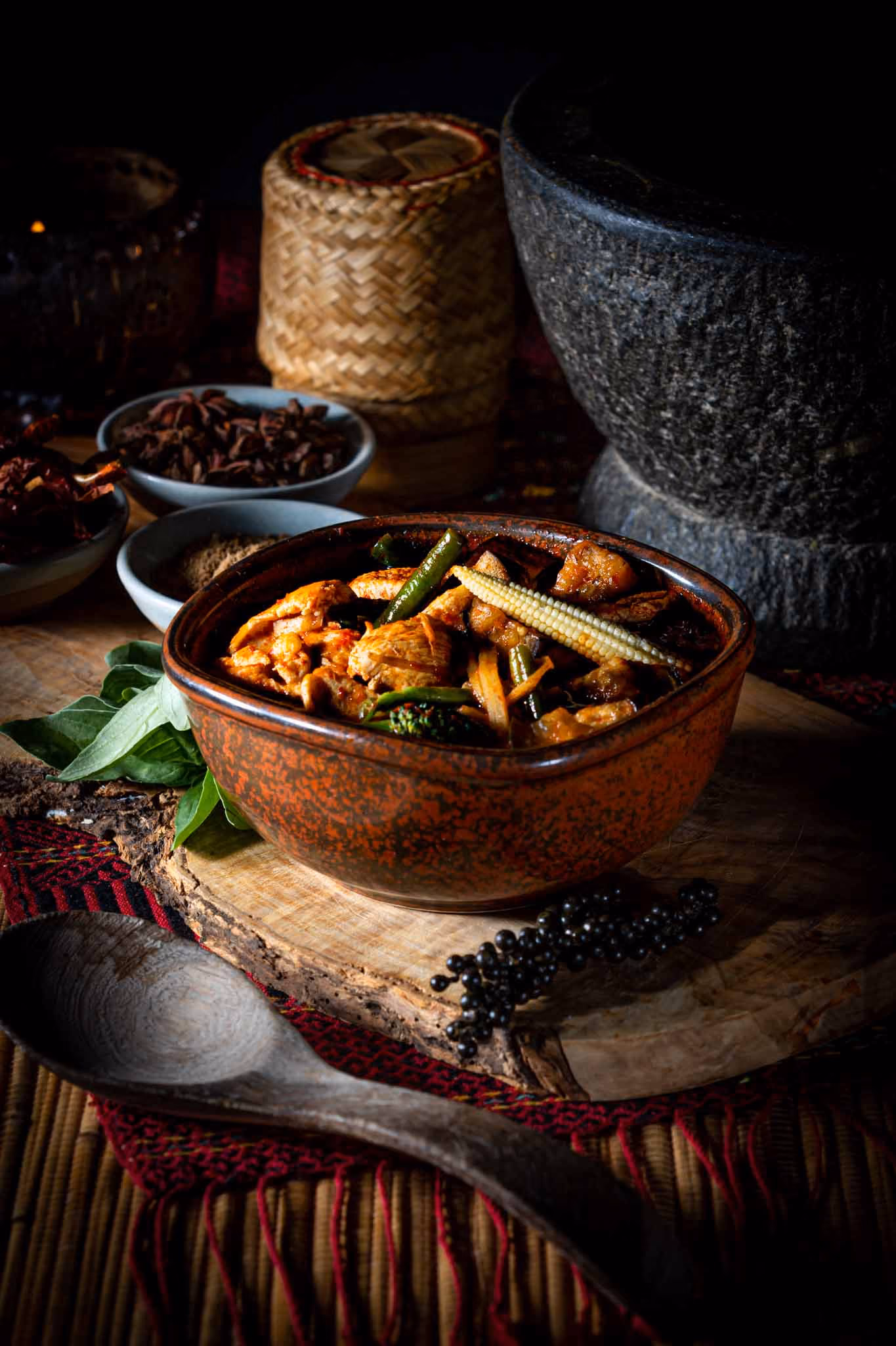 Thai jungle curry in a rustic bowl beside a granite pestle and mortar, dark food photography — by AlTopping.com