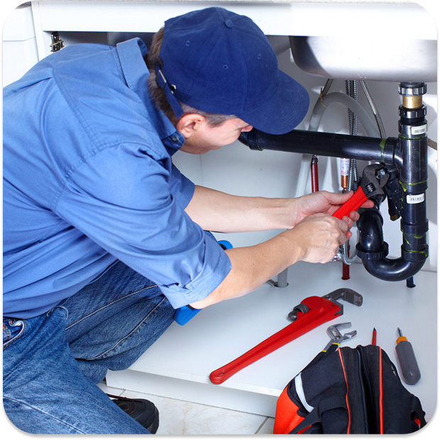 Klempner in blauer Arbeitskleidung repariert Rohr unter einer Spüle mit einer Wasserpumpenzange.