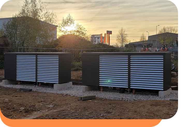 Zwei große Lüftungseinheiten mit grauen Lamellen auf einem Kiesbett im Freien bei Sonnenuntergang.