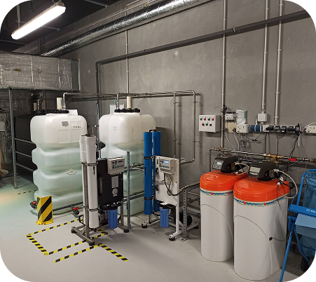 Wasseraufbereitungsanlage mit zwei großen weißen Tankbehältern, Rohren, Messgeräten und zwei Zylindern mit orangen Deckeln in einem Industrie-Umgebungsraum.