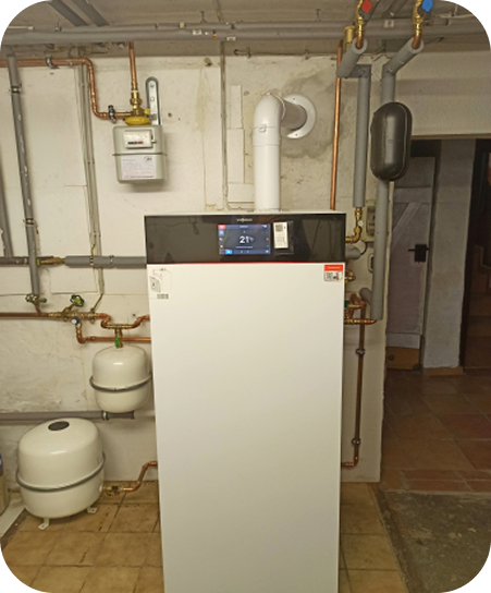 Heizungsanlage mit weißen und schwarzen Komponenten sowie Kupferrohren an einer weißen Wand.