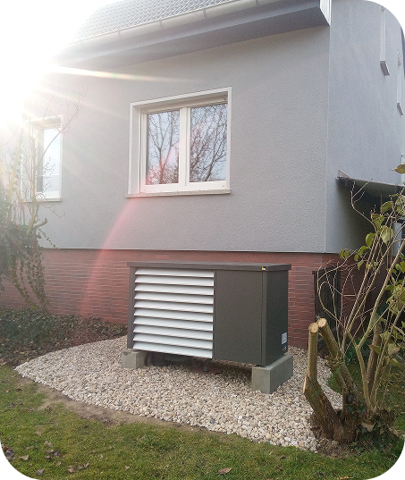 Außenansicht eines modernen Hauses mit einer Wärmepumpe auf Kies vor der Fassade bei Sonnenschein.