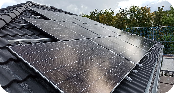 Solarmodule auf einem schwarzen Dach mit bewölktem Himmel und Bäumen im Hintergrund.
