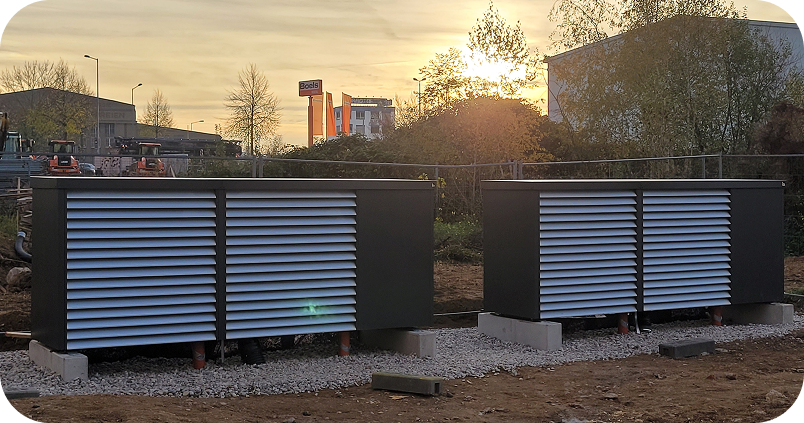 Zwei große schwarze Lüftungseinheiten auf Betonpfeilern auf einem Kiesbett im Freien bei Sonnenuntergang.