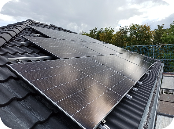 Solarpaneele auf einem schwarzen Ziegeldach unter bewölktem Himmel.