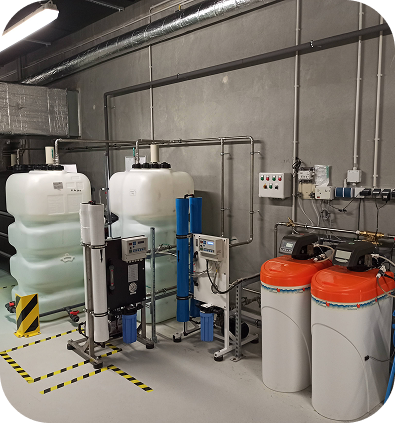 Industrielle Wasseraufbereitungsanlage mit großen weißen und blauen Filtern und Behältern in einem grauen Raum.