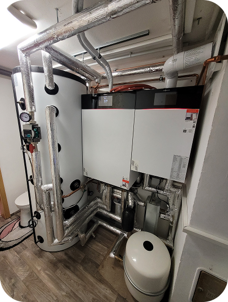 Moderne Heizungsanlage mit isolierten Rohren, Zylinder-Tank, Steuerungseinheit und Druckausgleichsbehälter in einem Technikraum.