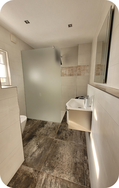 Modernes Badezimmer mit großem Spiegel, Waschtisch, frosted Glasdusche und dunklem Bodenbelag.