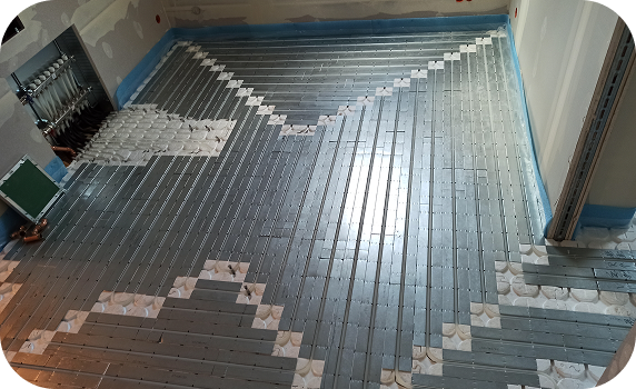 Fußbodenheizung mit Aluminiumleitblechen und Rohren in einem Raum im Rohbau installiert.