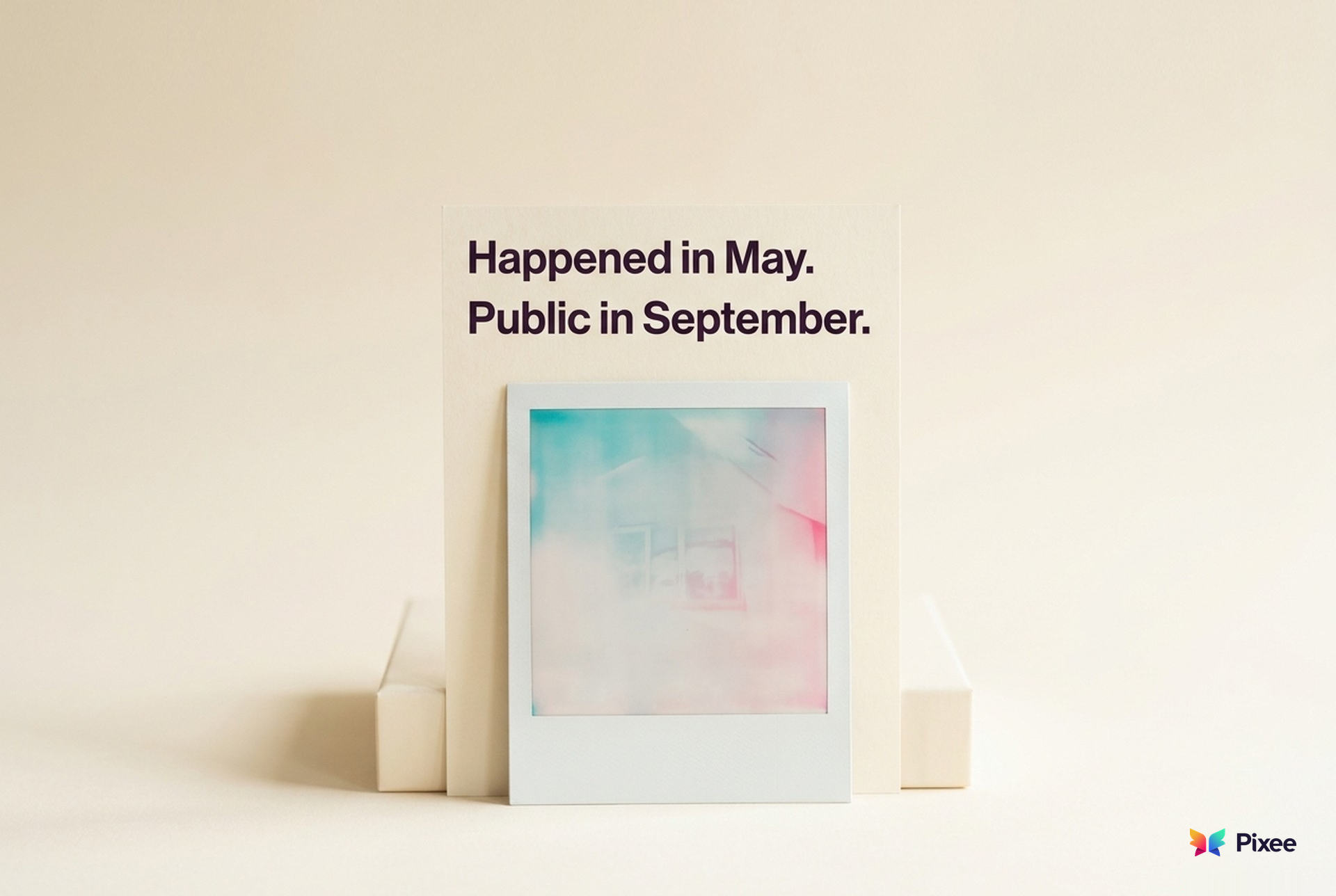 An instant photo still developing, propped in front of a card that reads Happened in May. Public in September.