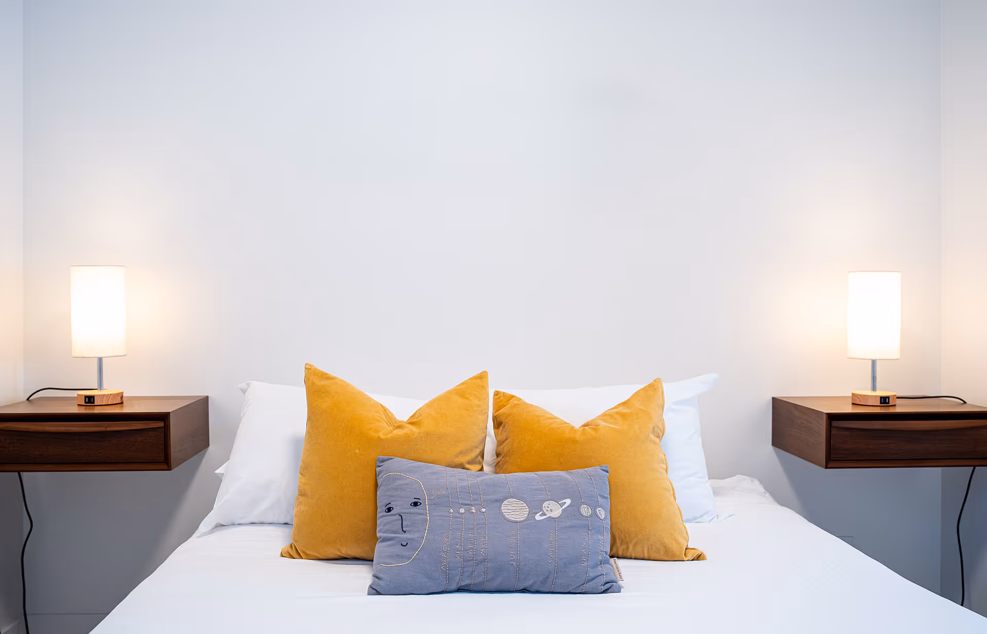 Clean bedroom, with side tables, lamps, made bed with yellow and blue pillows 